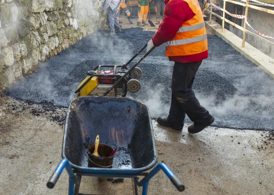 A construction worker forming the newly poured asphalt chemical.
