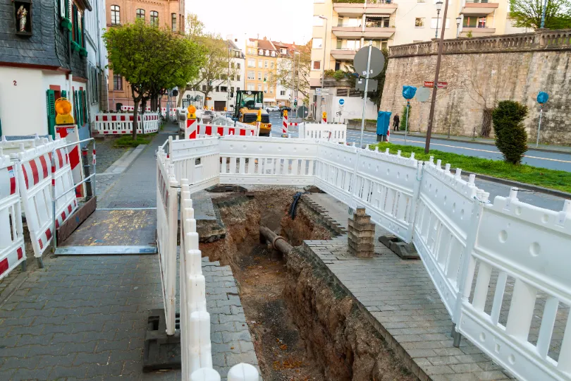 Deep trench dug for underground utility installation along a roadway under construction.