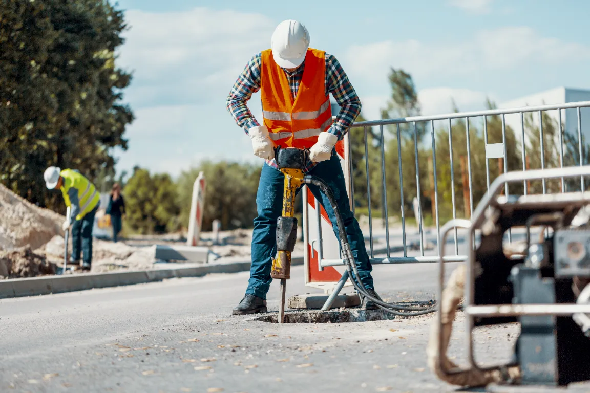 A worker with reflective vest drilling and repairing the concrete pavement.